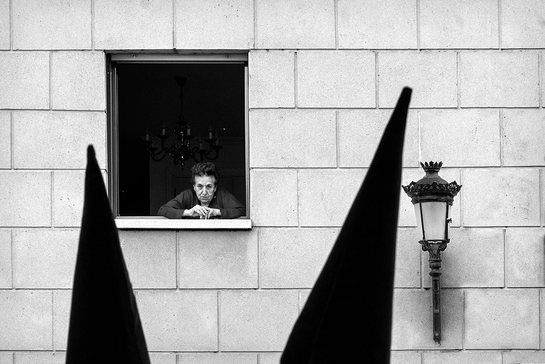 Capirotes oscuros en primer plano y una persona en una ventana.
